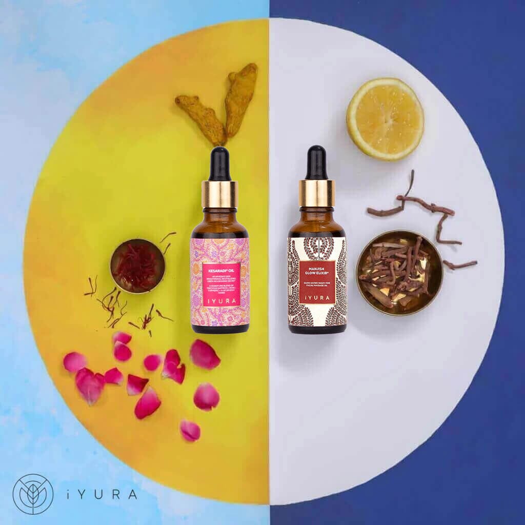 Day & Night Face Oil Duo, moisturizers for healthy skin by iYURA: the 1 fl oz (30 ml) Kesaradi Oil and Manjish Glow Elixir dropper bottles on a circle split into a yellow half, with turmeric roots, saffron and rose petals, and a white half, with half a lemon and a bowl of dried red roots, on a blue background with the iYURA logo