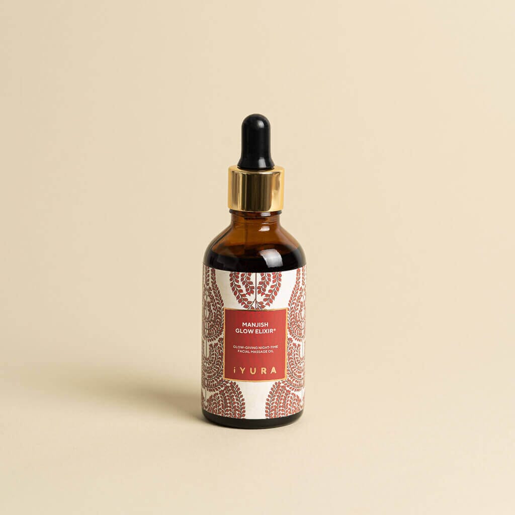 Manjish Glow Night Time Elixir bottle on a plain beige background. Label: Manjish Glow Elixir®. Glow-giving night-time facial massage oil. iYURA