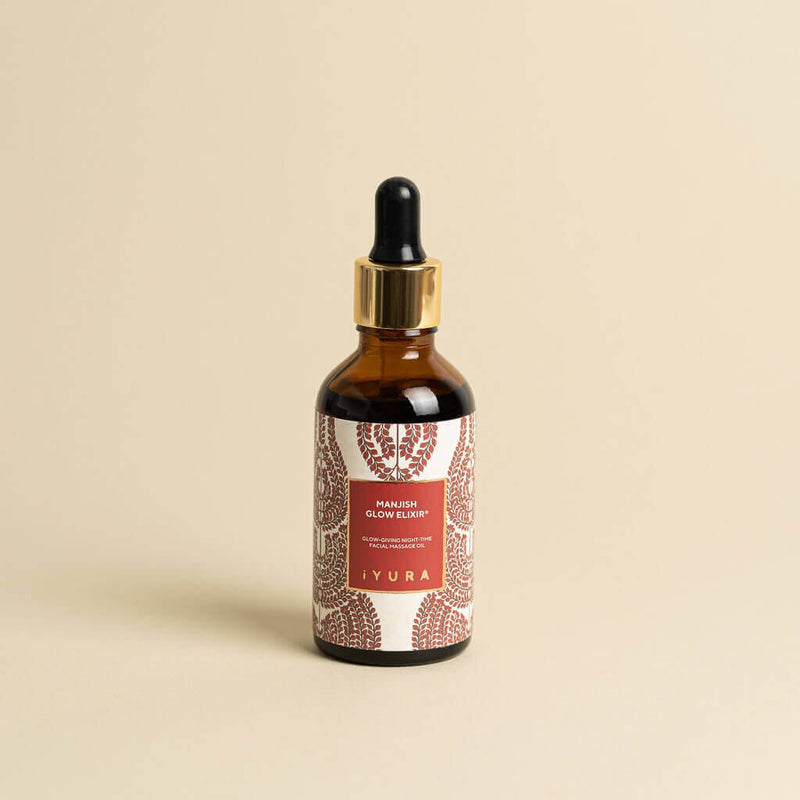 Manjish Glow Night Time Elixir bottle on a plain beige background. Label: Manjish Glow Elixir®. Glow-giving night-time facial massage oil. iYURA