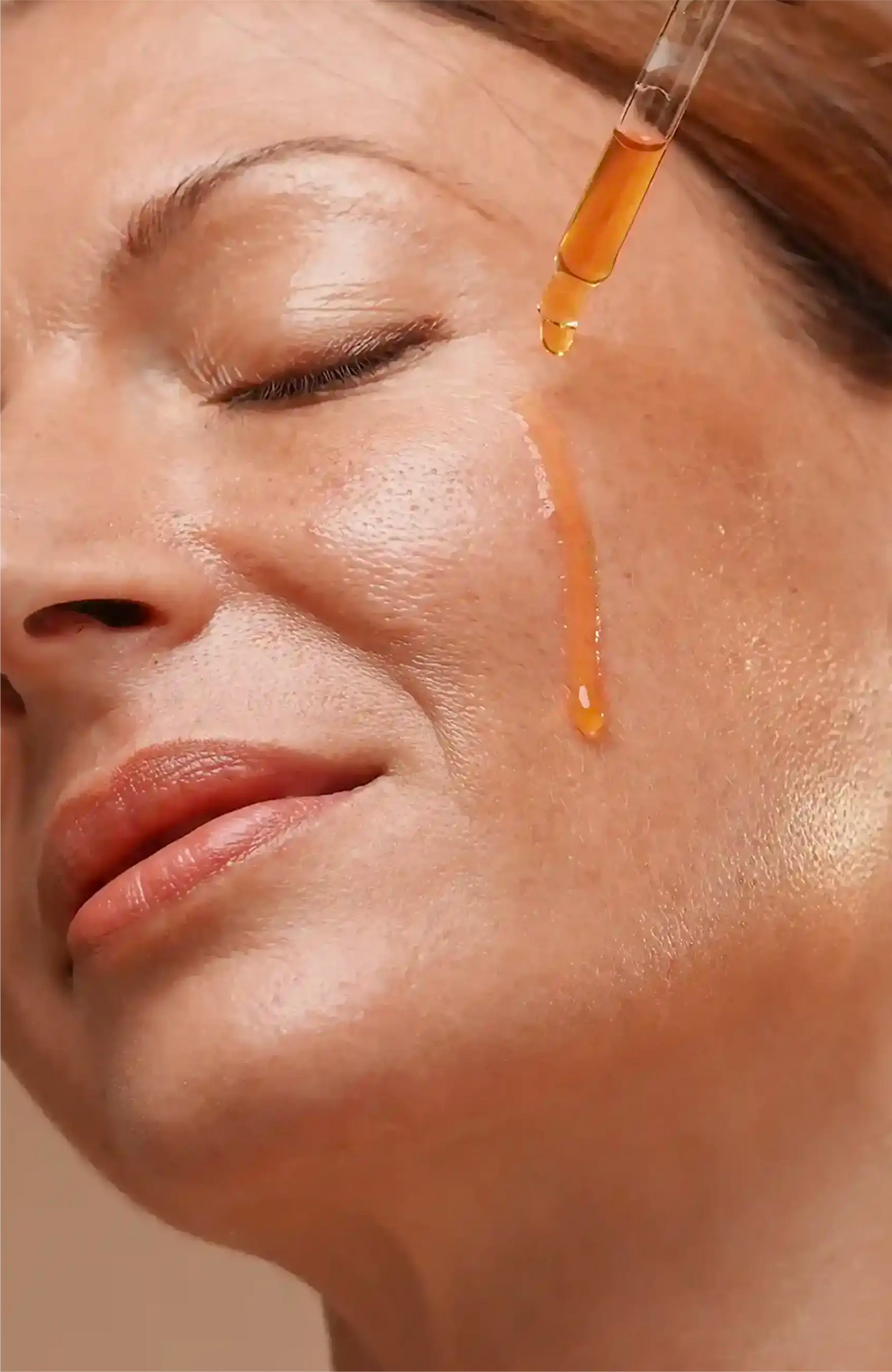 Manjish Glow Night Time Elixir: drops of the golden oil from a dropper running down a woman’s cheek