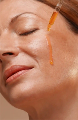 Manjish Glow Night Time Elixir: drops of the golden oil from a dropper running down a woman’s cheek