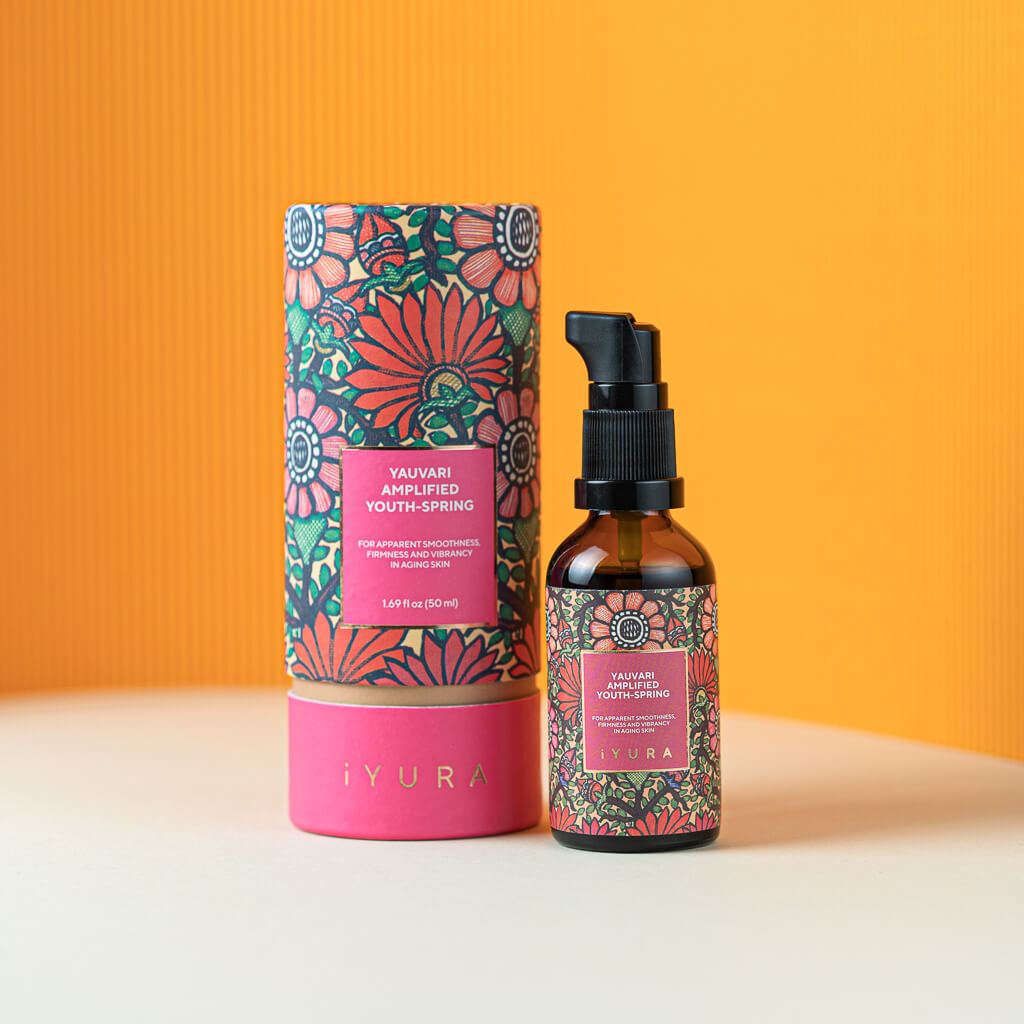 Black Gram Face & Body Duo: the Yauvari Amplified Youth Spring bottle and tube against an orange wall. Label: for apparent smoothness, firmness and vibrancy in aging skin, 1.69 fl oz (50 ml)
