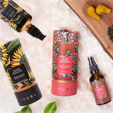 Black Gram Face & Body Duo: the Balaayah Black Gram Body Booster bottle and tube and the Yauvari Amplified Youth Spring tube and bottle on a white fluffy rug, beside turmeric root and black gram on a wooden board