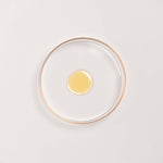 Kesaradi Daily Glow Oil texture: a drop of the pale golden oil in a glass dish with a rose-gold rim, on a white background